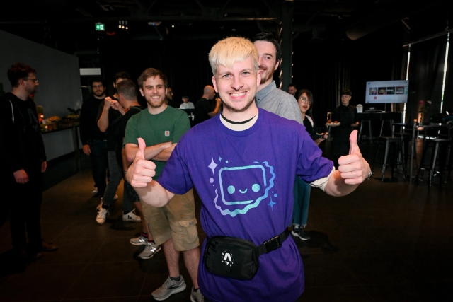 Alex, a maintainer, poses with two thumbs up while wearing a purple Houston printed t-shirt.