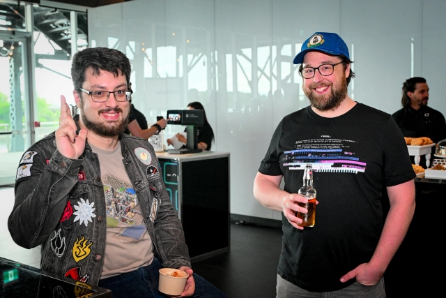 Two glasses-wearing male guests smile and pose together with their food and drink.