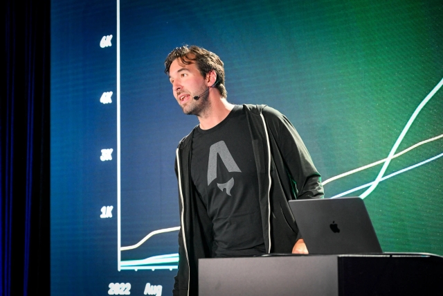 Fred K. Schott on stage in front of a slide depicting a graph, standing next a podium with a laptop sitting atop it.