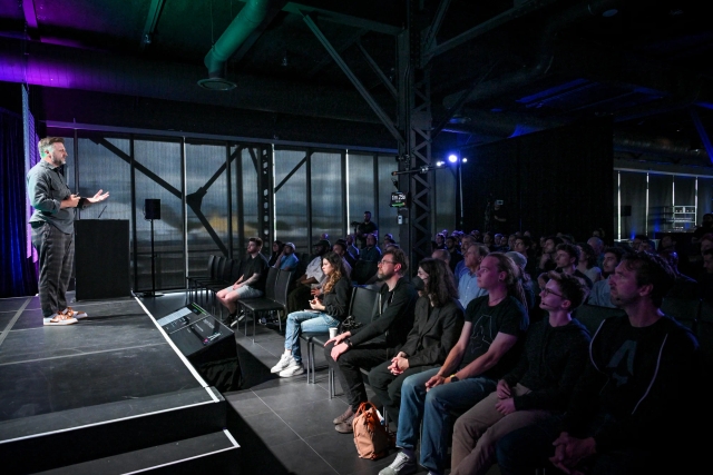 Side stage view of Matthew Phillips speaking on stage, addressing the crowd.