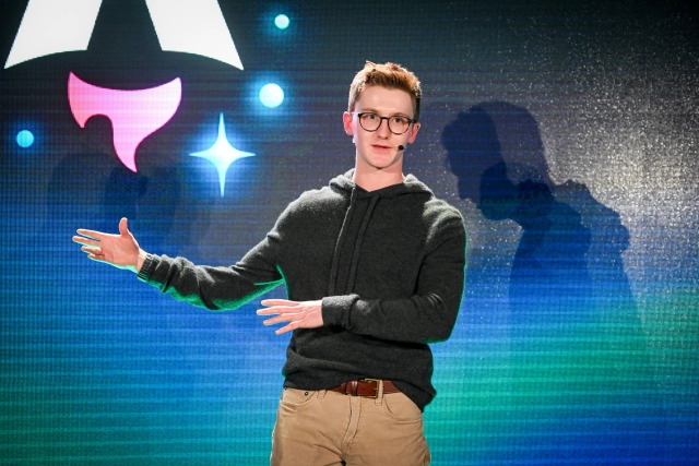 Closeup of Ben Holmes on stage with hands outstretched to his right as he answers an audience member question.