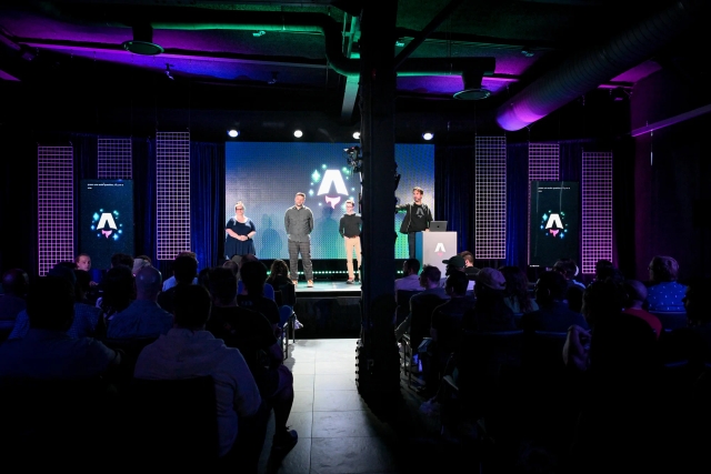 View from the back of the audience. Keynote speakers on stage. From left to right: Sarah Rainsberger, Matthew Phillips, Ben Holmes, and Fred K. Schott (next to the podium).